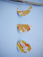 Close up on moon phases paper garland. Hand-painted with yellow, orange and gold ink this decorative yelllow paper garland creates a full moon phases wall hanging