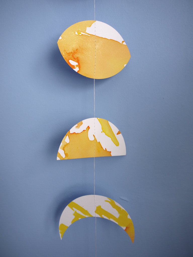 Close up on a Flower Moon phases wall hanging. Eco friendly decor hand-painted with yellow, orange and gold ink. Decorative paper garland for May birthday gift