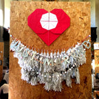 Wedding decor display at a wedding market at "St. Andrew's on the square", Glasgow. A giant origami heart; below a white tissue tassel garland with pastel paper garland and a "JUST MARRIED" banner in front of it