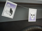 Close up of a cat and a skull Illustrated riso printed stitched Halloween paper garland in black white and purple hanging above a grey and black fireplace