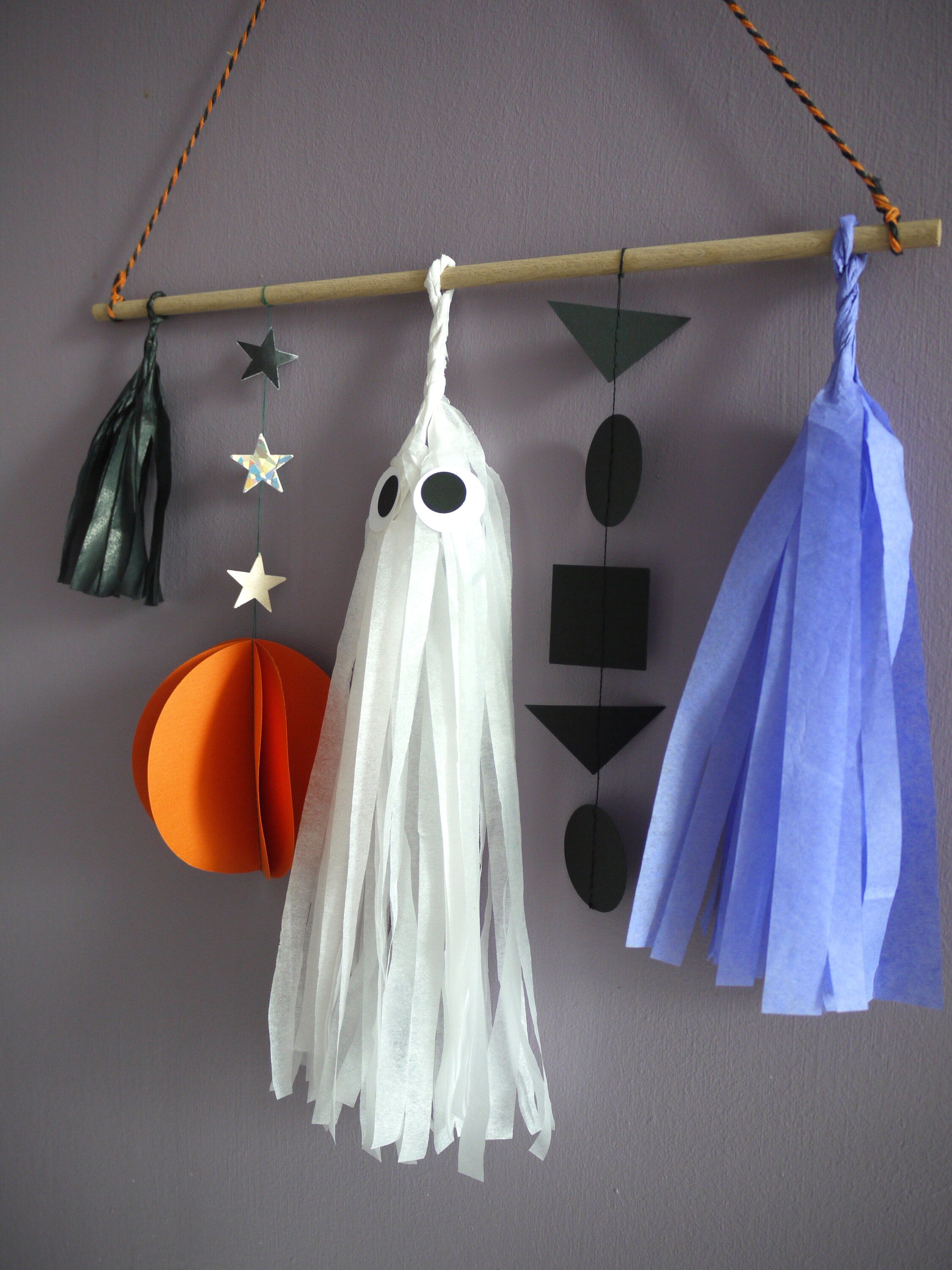 Close up on black, orange, lilac and white ghost paper decorations of the Halloween scene wall hanging
