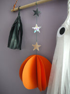 Close up on black, orange with holographic stars and white ghost paper decorations of the Halloween scene wall hanging