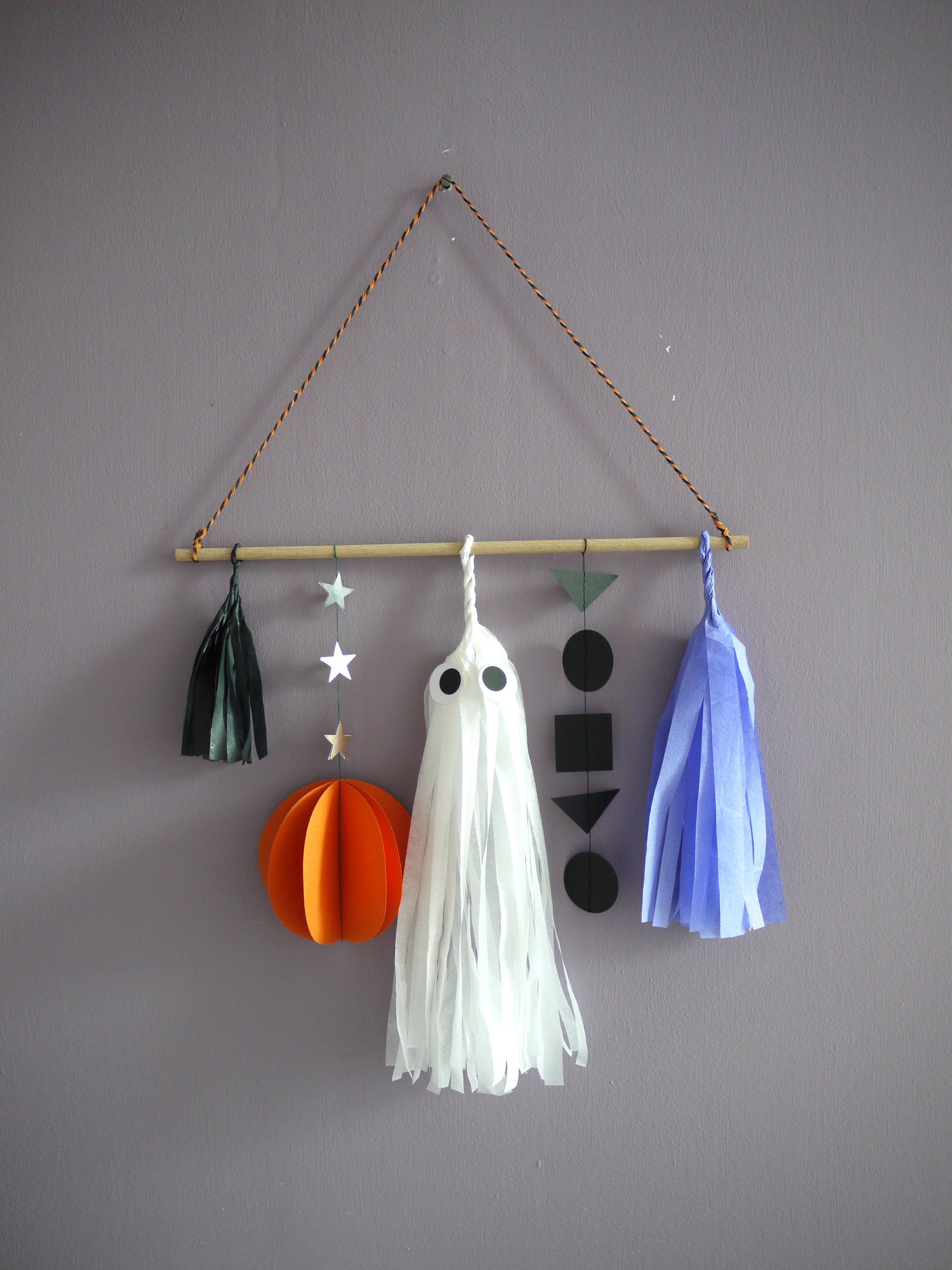 Abstract Halloween scene wall hanging with black, orange, white and lilac paper decorations showing garland, tassels, a pumpkin and a ghost