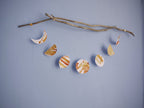 Horizontal moon phase shapes painted with golden tans and brown ink stitched to create a wall hanging displayed on a blue background