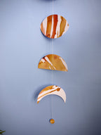 Moon phase stitched garland painted with golden tans and brown ink stitched to create a wall hanging displayed on a blue background