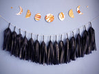 Horizontally displayed moon phases stitched garland painted with golden tans and brown ink stitched to create a wall hanging on a blue background wh navy blue tissue tassel garland below