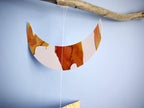 Close up of moon phases stitched garland painted with golden tan and brown inks displayed as a wall hanging on a blue background 