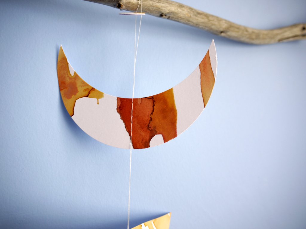 Close up of moon phases stitched garland painted with golden tan and brown inks displayed as a wall hanging on a blue background 