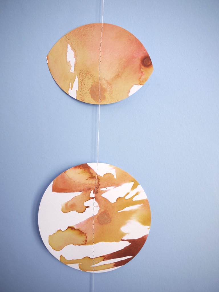 Close up of moon phases stitched garland painted with golden tan and brown inks displayed as a wall hanging on a blue background 