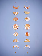 Two moon phases stitched garlands painted slightly differently with golden tan and brown inks displayed as a wall hanging on a blue background 