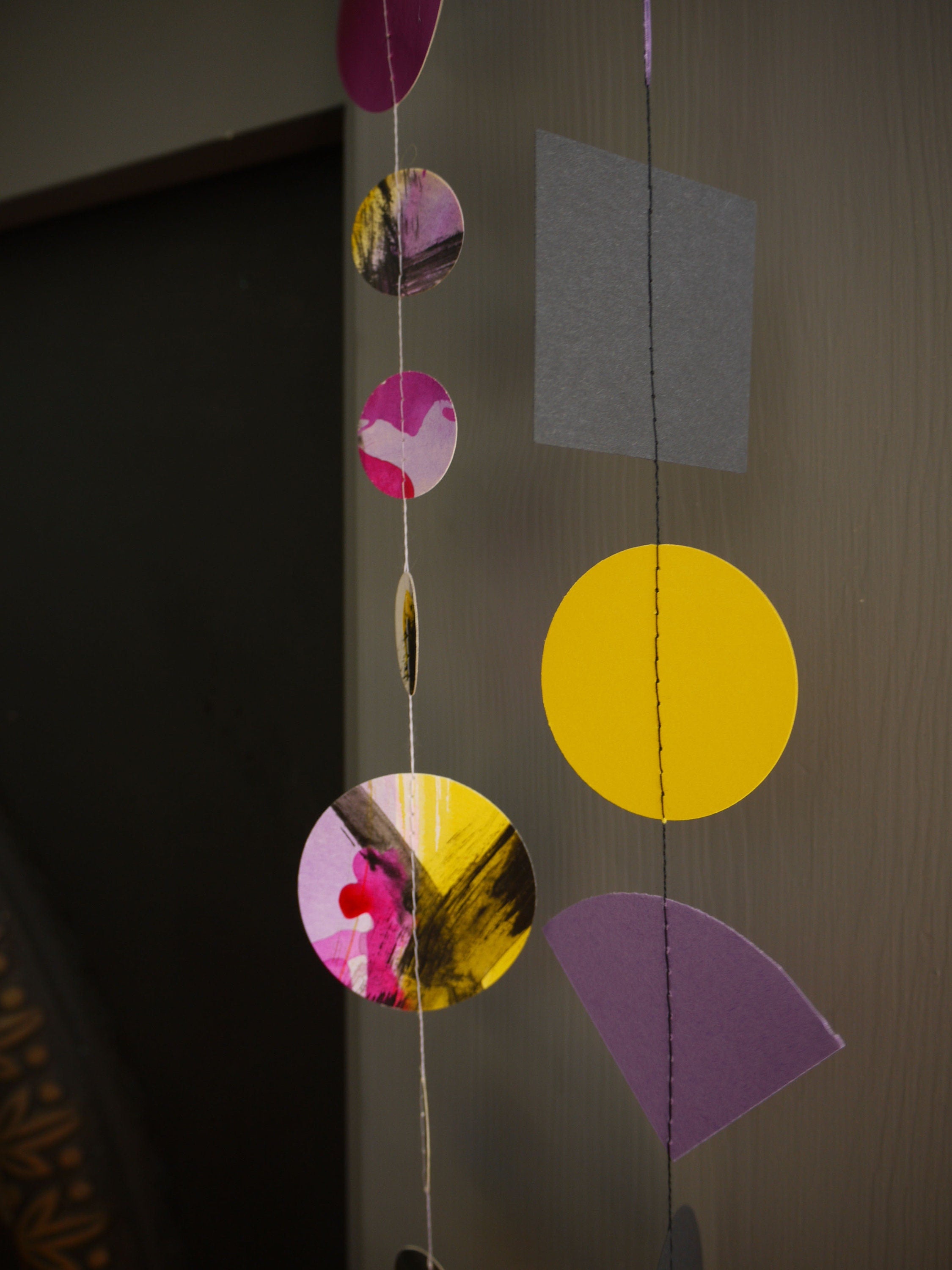 Close up on paper garlands from Paper Street Dolls Jem collection. At a fireplace sits a multishape garland in bold tones, below a painted circle garland 