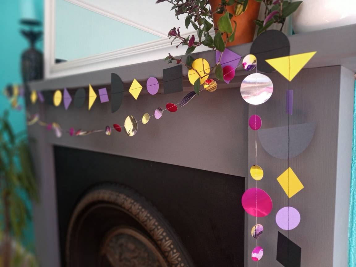 Close up on paper garlands from Paper Street Dolls Jem collection. At a fireplace sits a multishape garland in bold tones, below a painted circle garland 