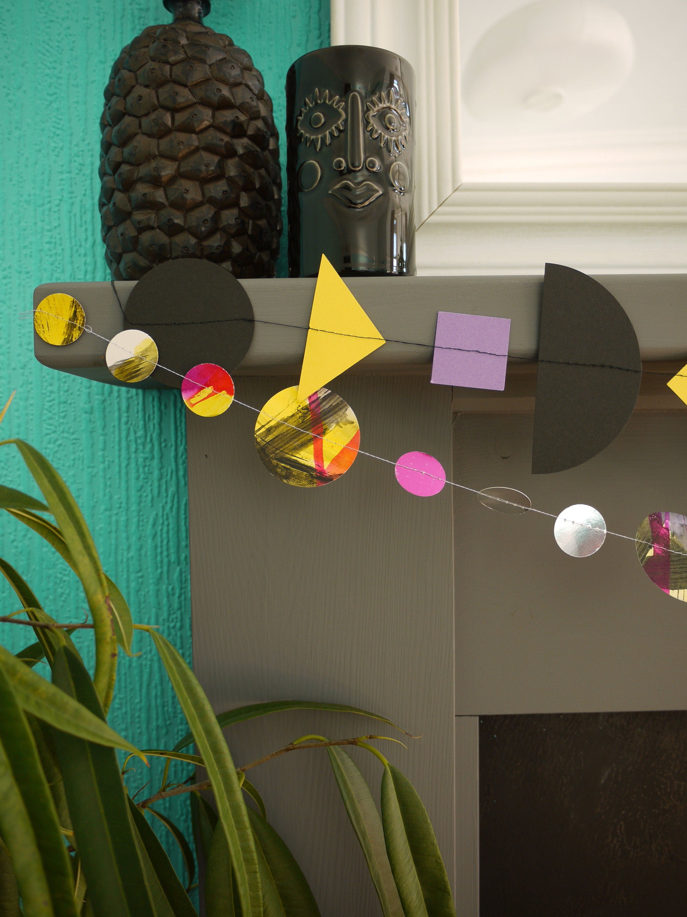 Close up on paper garlands from Paper Street Dolls Jem collection. At a fireplace sits a multishape garland in bold tones, below a painted circle garland 