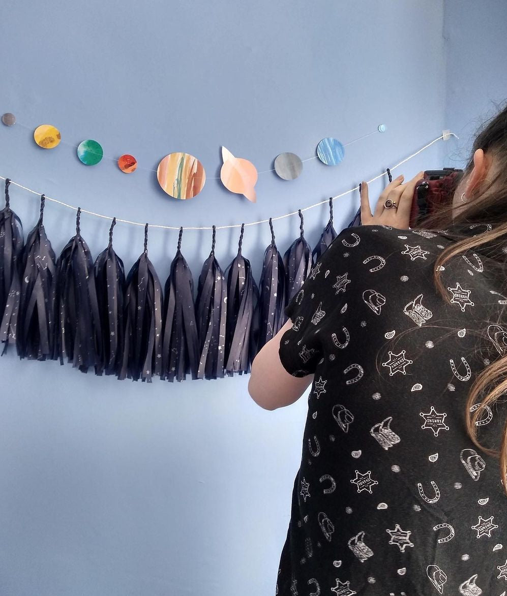 Person taking a photo of a decorative wall with tassels and colorful solar system wall hanging