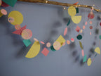 Pink, yellow, orange and turquoise marbled and geometric paper garlands wall display with driftwood and fairy lights