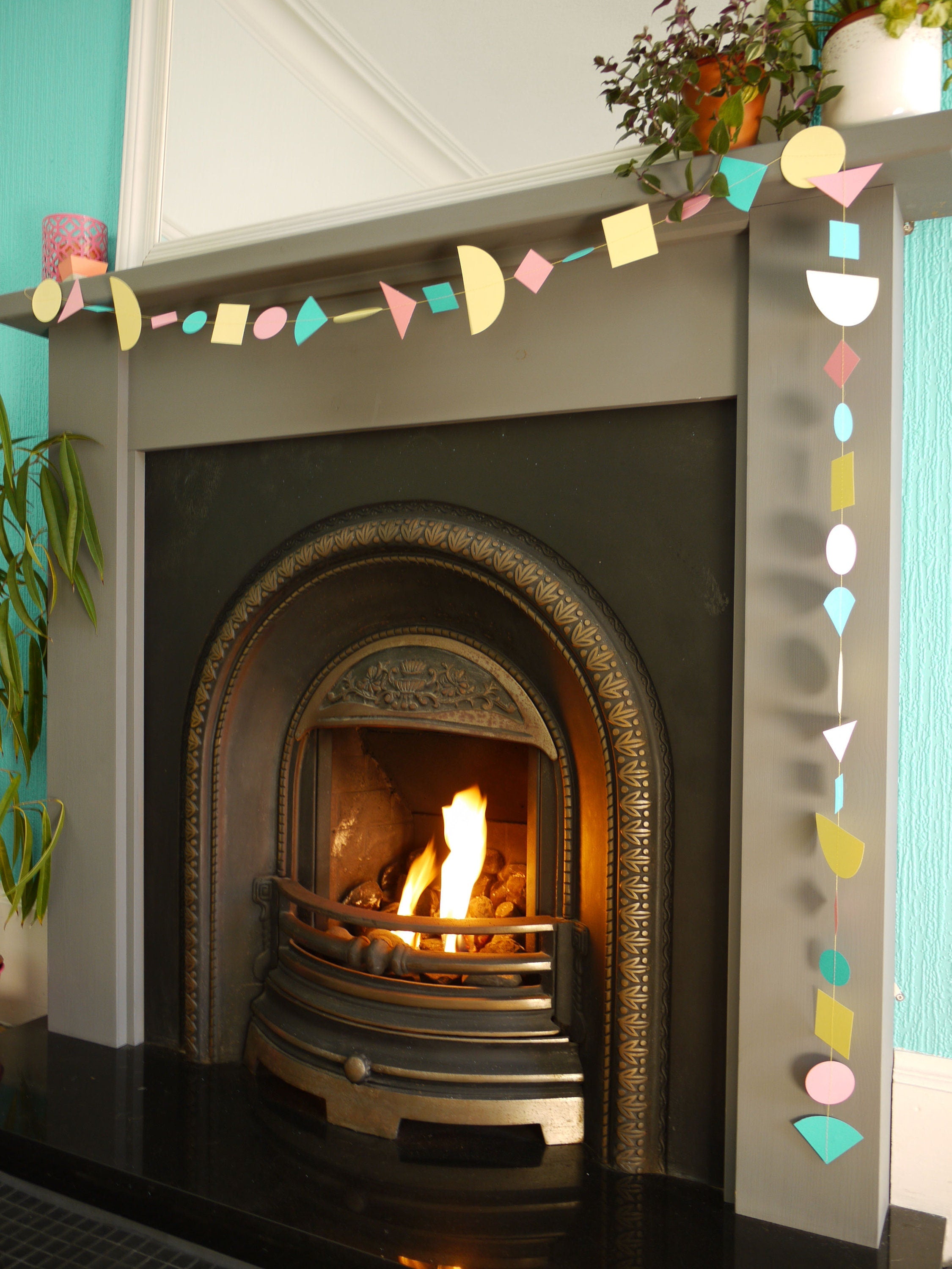 A fireplace display with modern multi shape paper garland in Paper Street Doll's LORELAI colours of aqua, lemon yellow and rose