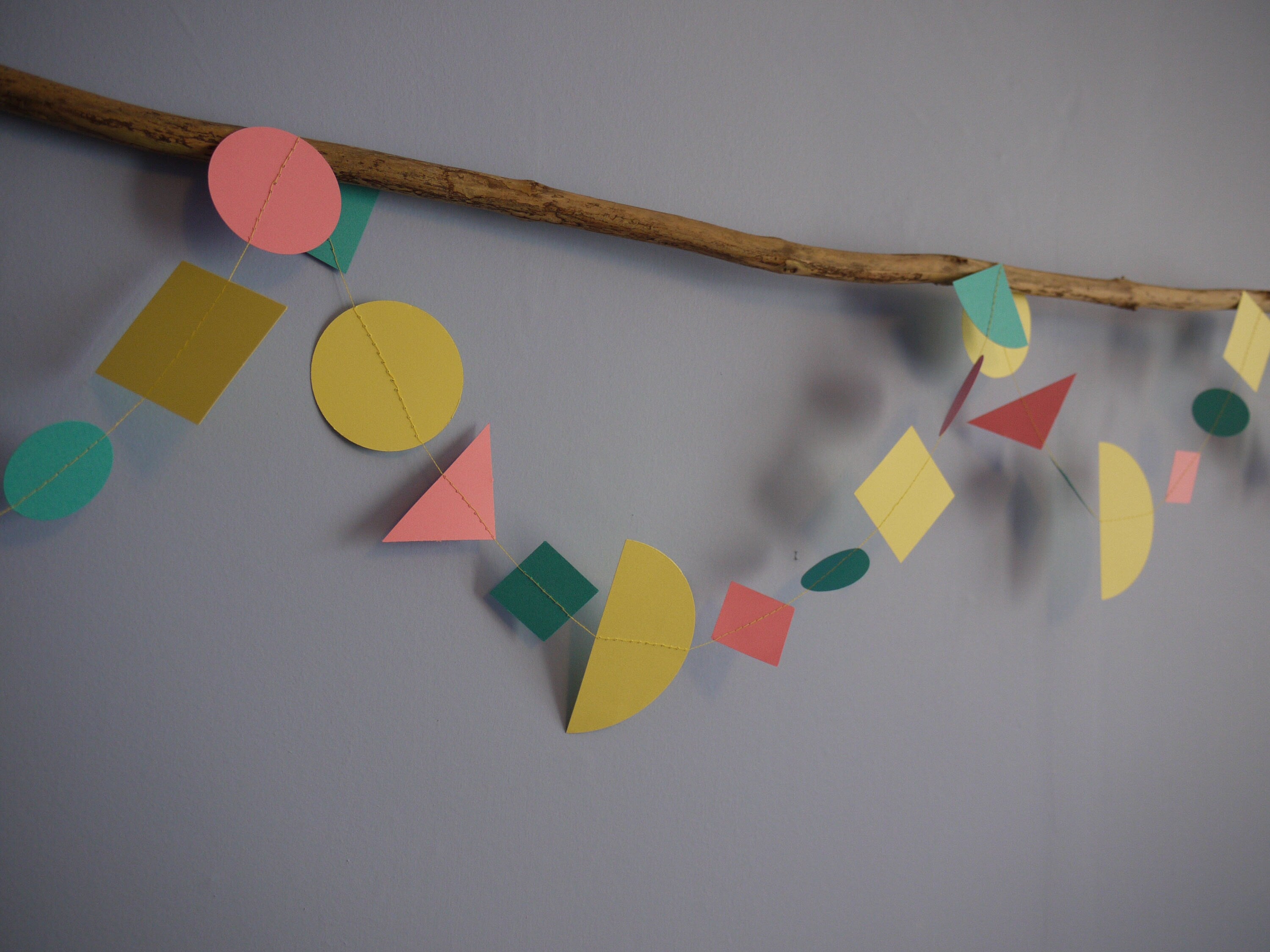 Home wall hanging on driftwood with modern multi shape paper garland in Paper Street Doll's LORELAI colours of aqua, lemon yellow and rose