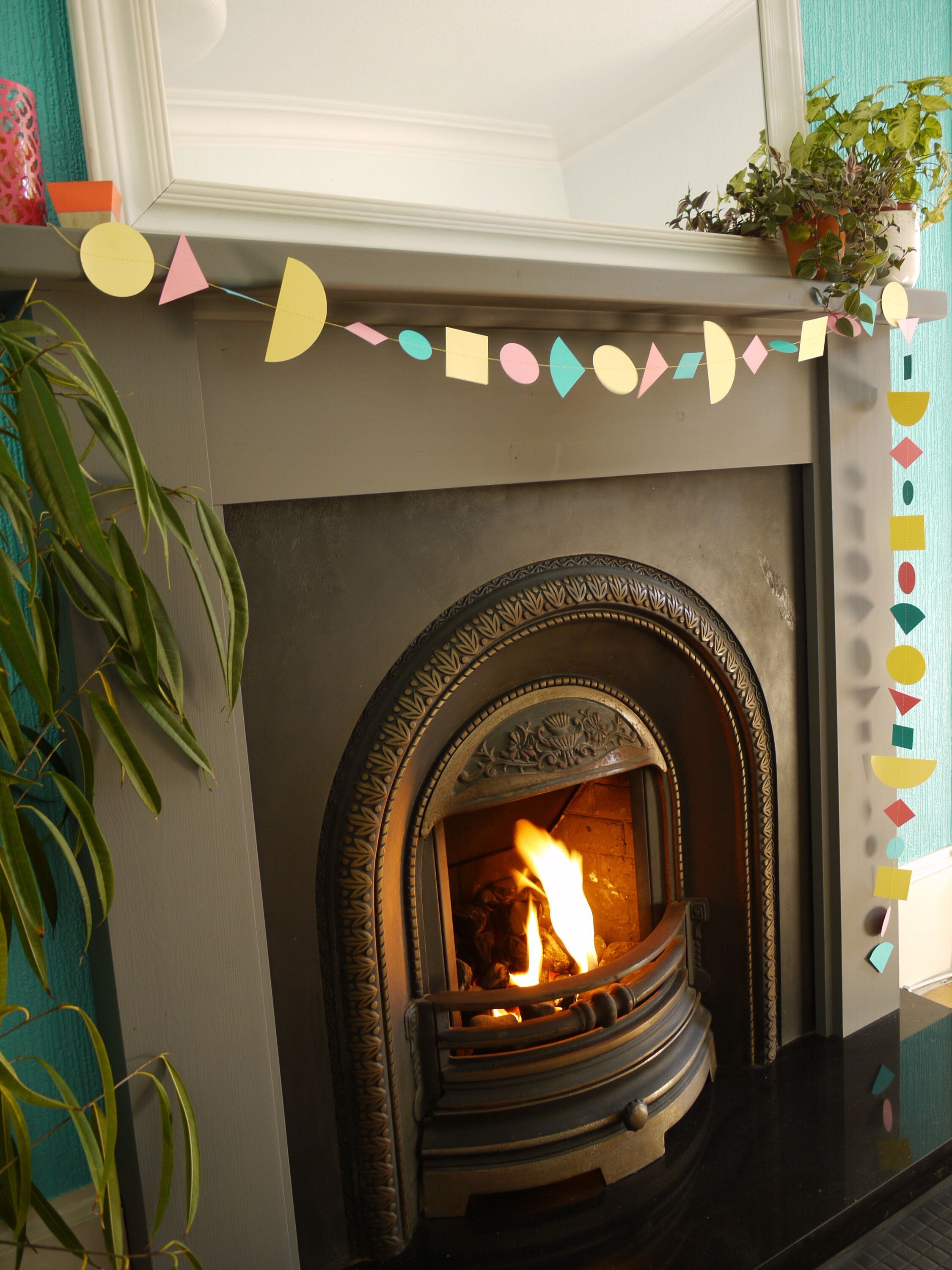 A living room fireplace with a modern multi shape paper garland in Paper Street Doll's LORELAI colours of aqua, lemon yellow and rose