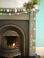 Geometric and watercolour paper garlands in Paper Street Doll's OPHELIA colours of grey, grass green and blue, displayed at a fireplace