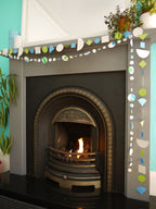 Geometric and watercolour paper garlands in Paper Street Doll's OPHELIA colours of grey, grass green and blue surround a fireplace