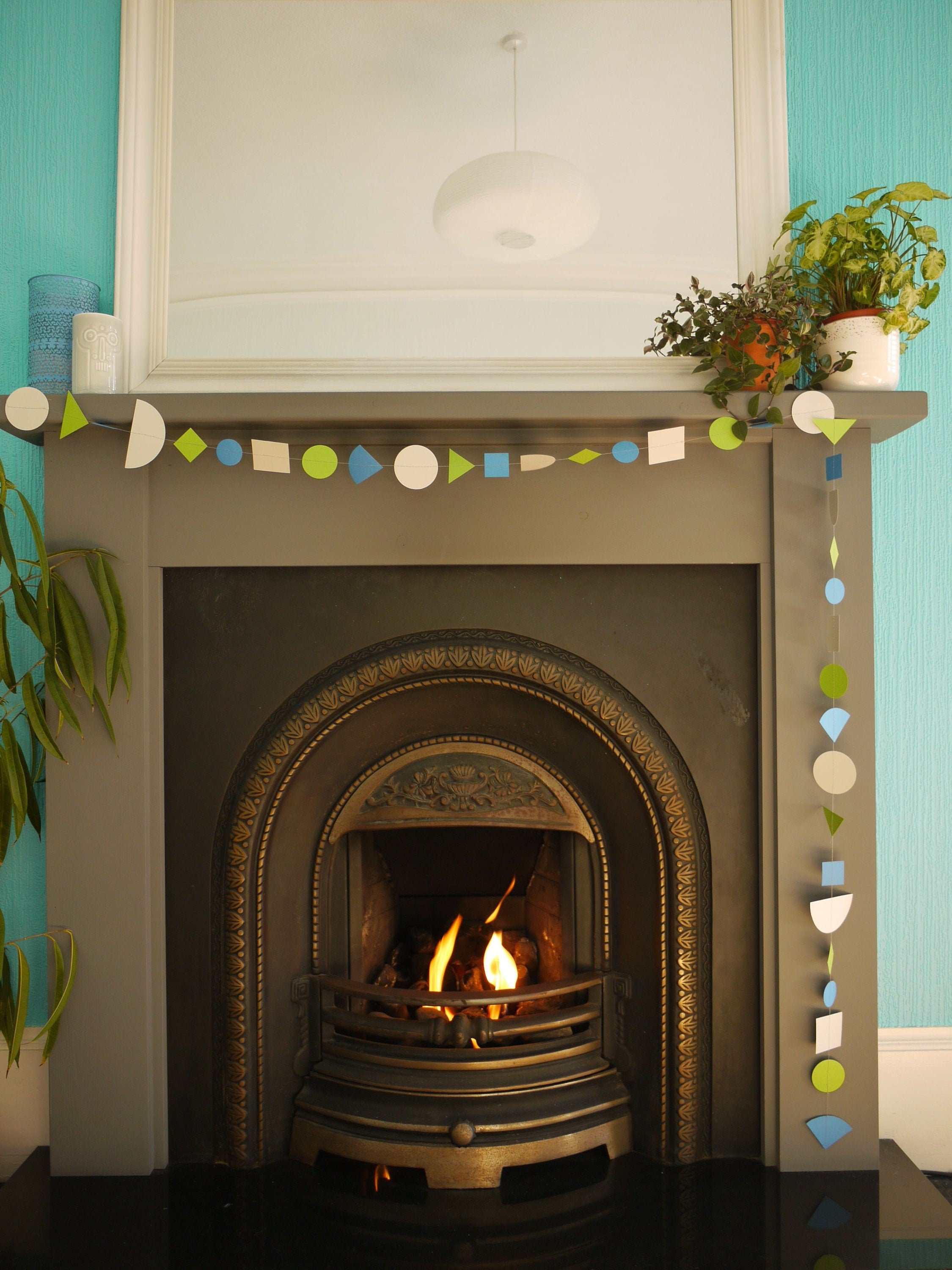 Modern multi shape paper garland in Paper Street Doll's OPHELIA colours of grey, grass green and blue at a fireplace