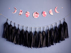 Moon phase shapes painted with pink and black ink stitched to create a wall hanging displayed on a blue background with navy blue constellation printed tissue paper tassel garland hanging underneath 