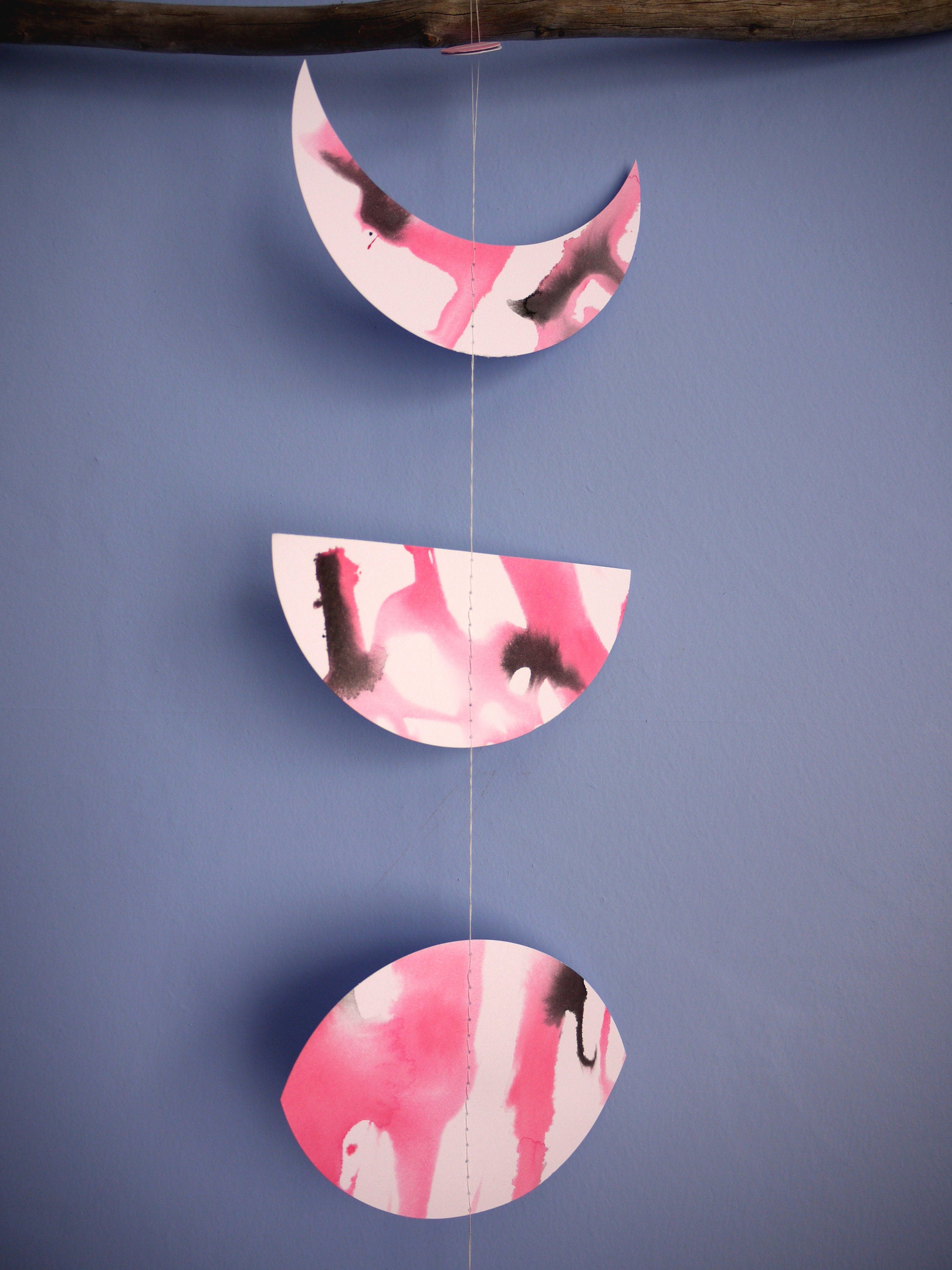 Close up of moon phase shapes painted with pink and black ink stitched to create a wall hanging displayed on a blue background 