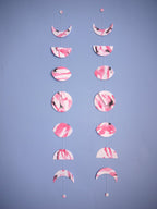 Two moon phase garlands painted slightly differently with pink and black ink stitched to create a wall hanging displayed on a blue background 