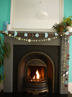 Paper garlands from Paper Street Dolls Ragnar collection. At a fireplace sits a multishape garland in cool tones, below a marbled circle garland 