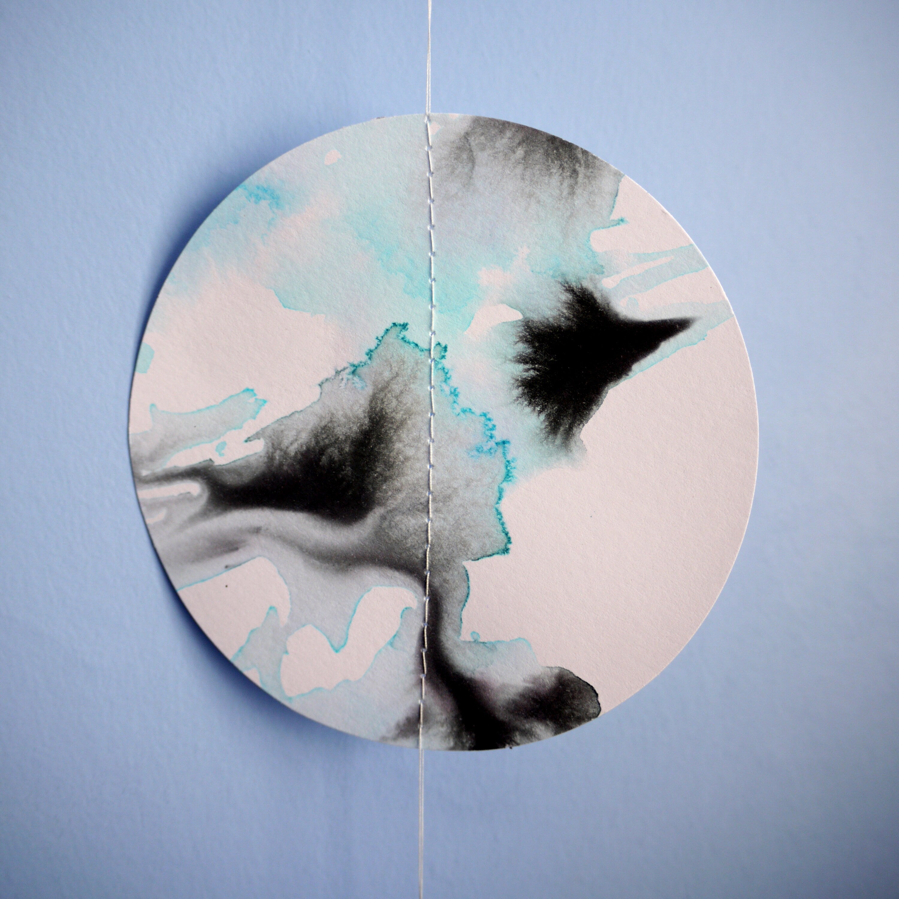 Close up of full moon shape wall paper garland painted with black and blue inks hung on on a blue wall