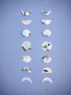 Two moon phases wall hangings stitched paper garland painted with black and blue inks hung on a blue wall