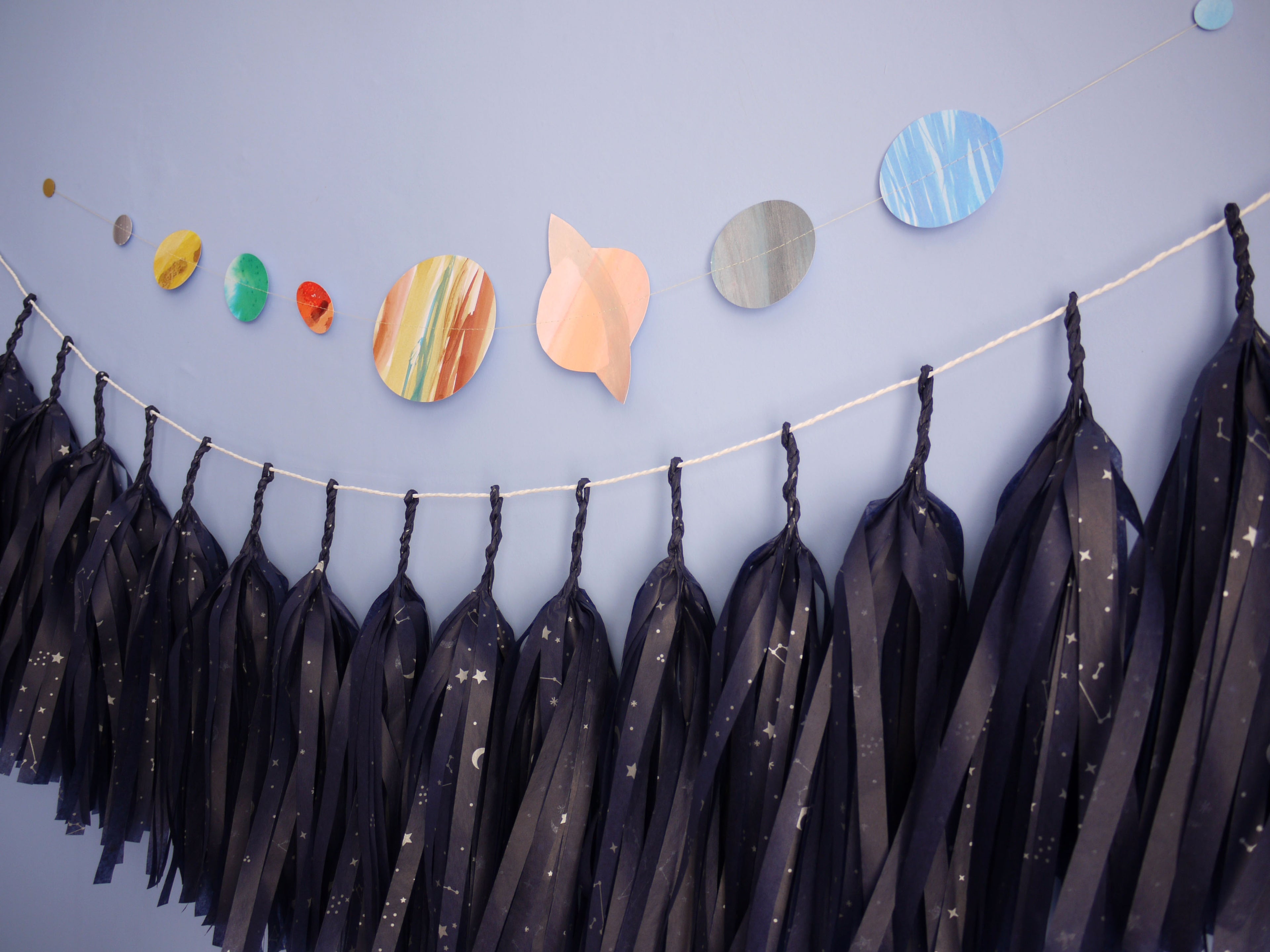 Decorative space-themed wall hanging with planet cutouts and tassel garland with constellation pattern.