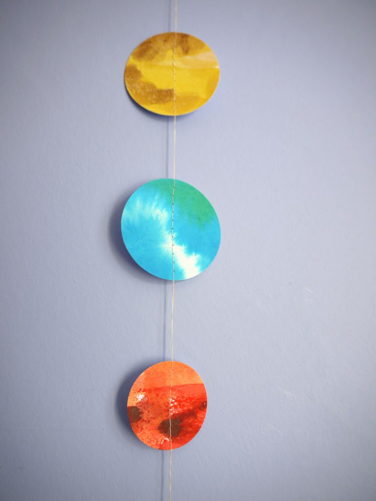 Colorful circular decorations on a string against a gray background - abstract paintings of planets as a paper garland.