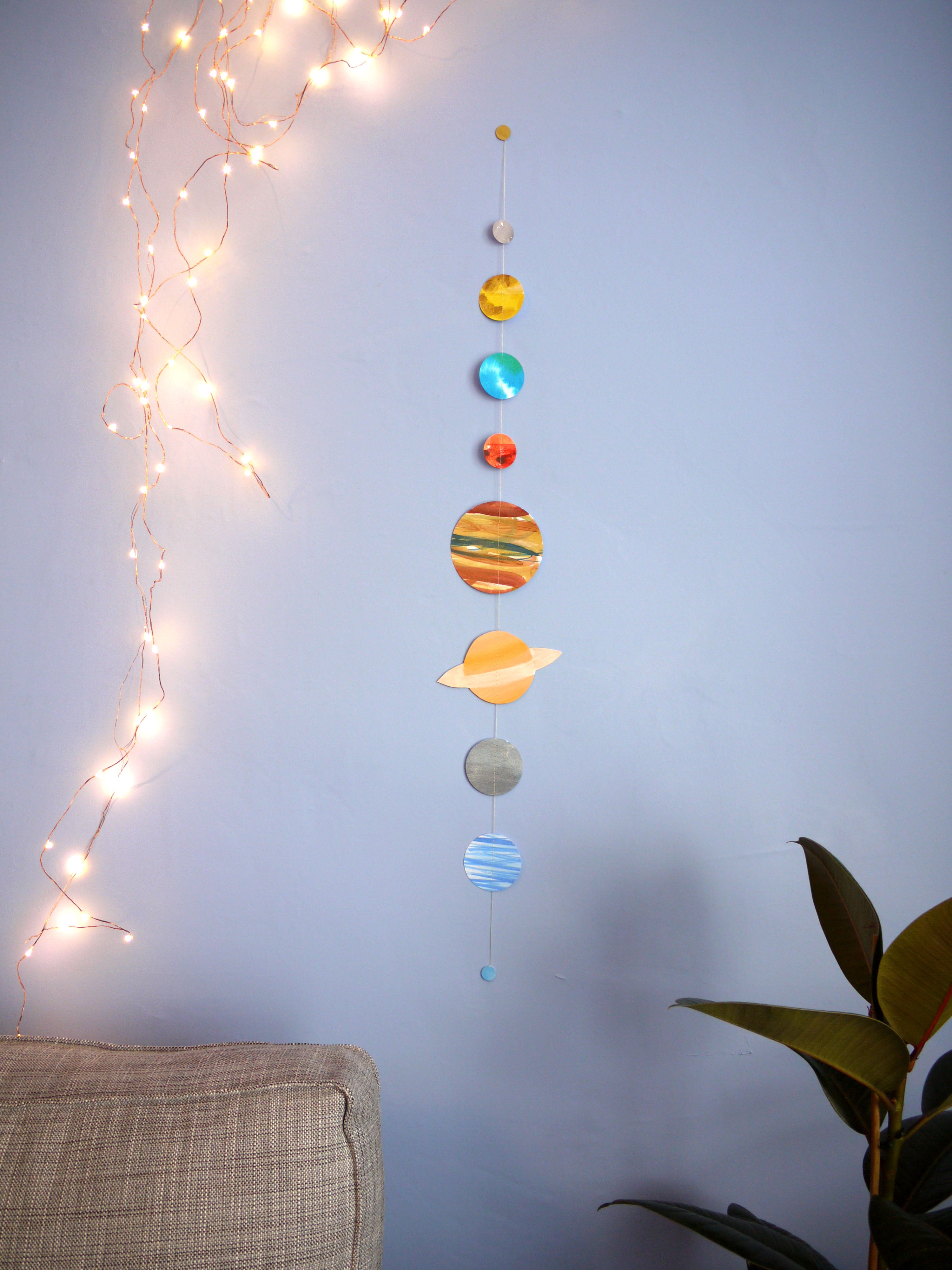 Decorative solar system model hanging on a wall with string lights and a plant.