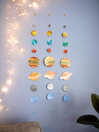 Decorative solar system mobiles with colorful planets hanging against a light blue wall. Three hanging for comparison of this unique painted wall hanging.