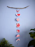 Pink and red moon phases paper garland hanging from driftwood surrounded by houseplants