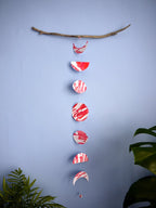 Pink and red moon phases paper garland hanging from driftwood surrounded by houseplants