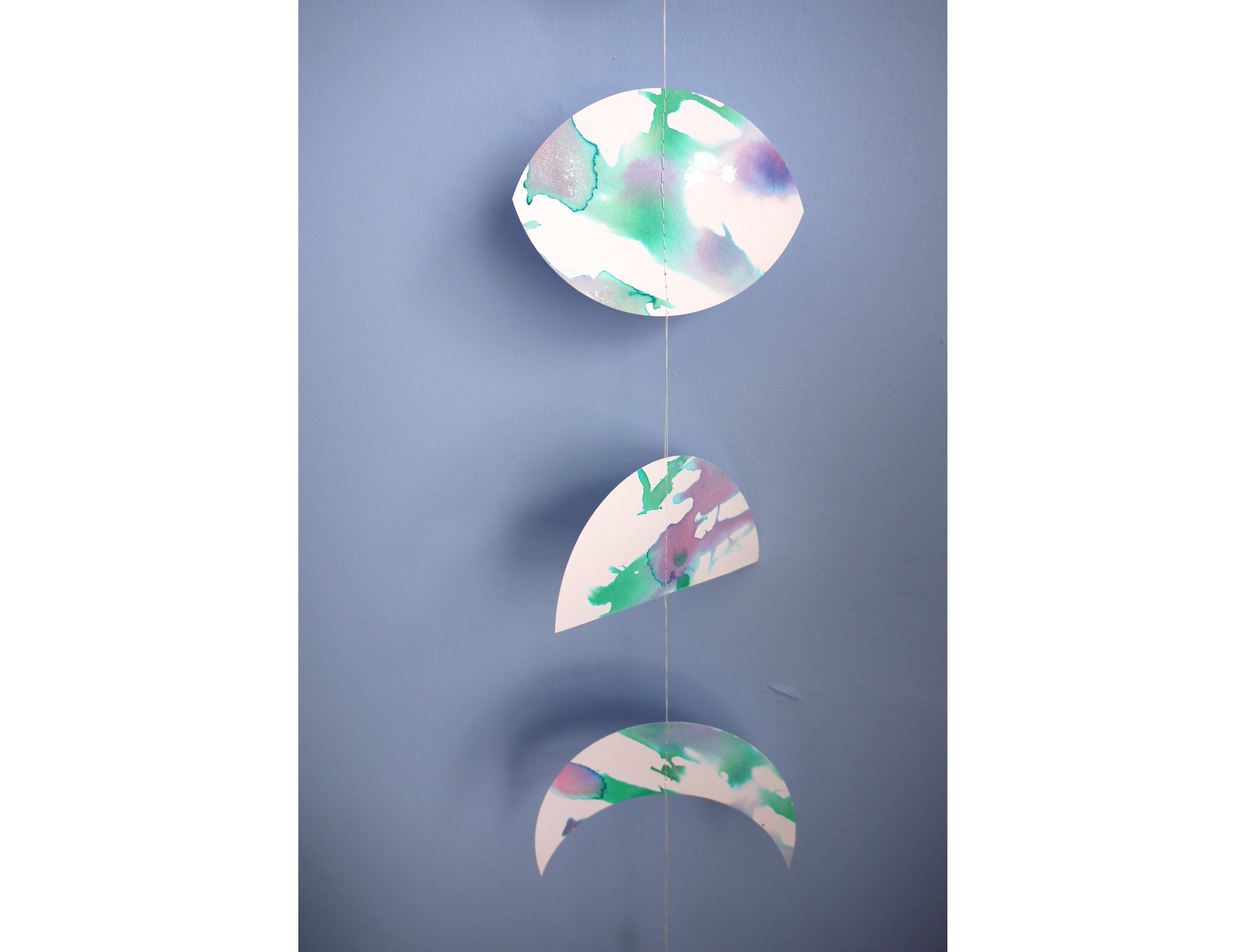 Close up of moon phase shapes painted with green and purple pearlised ink stitched to create a wall hanging displayed on a blue background