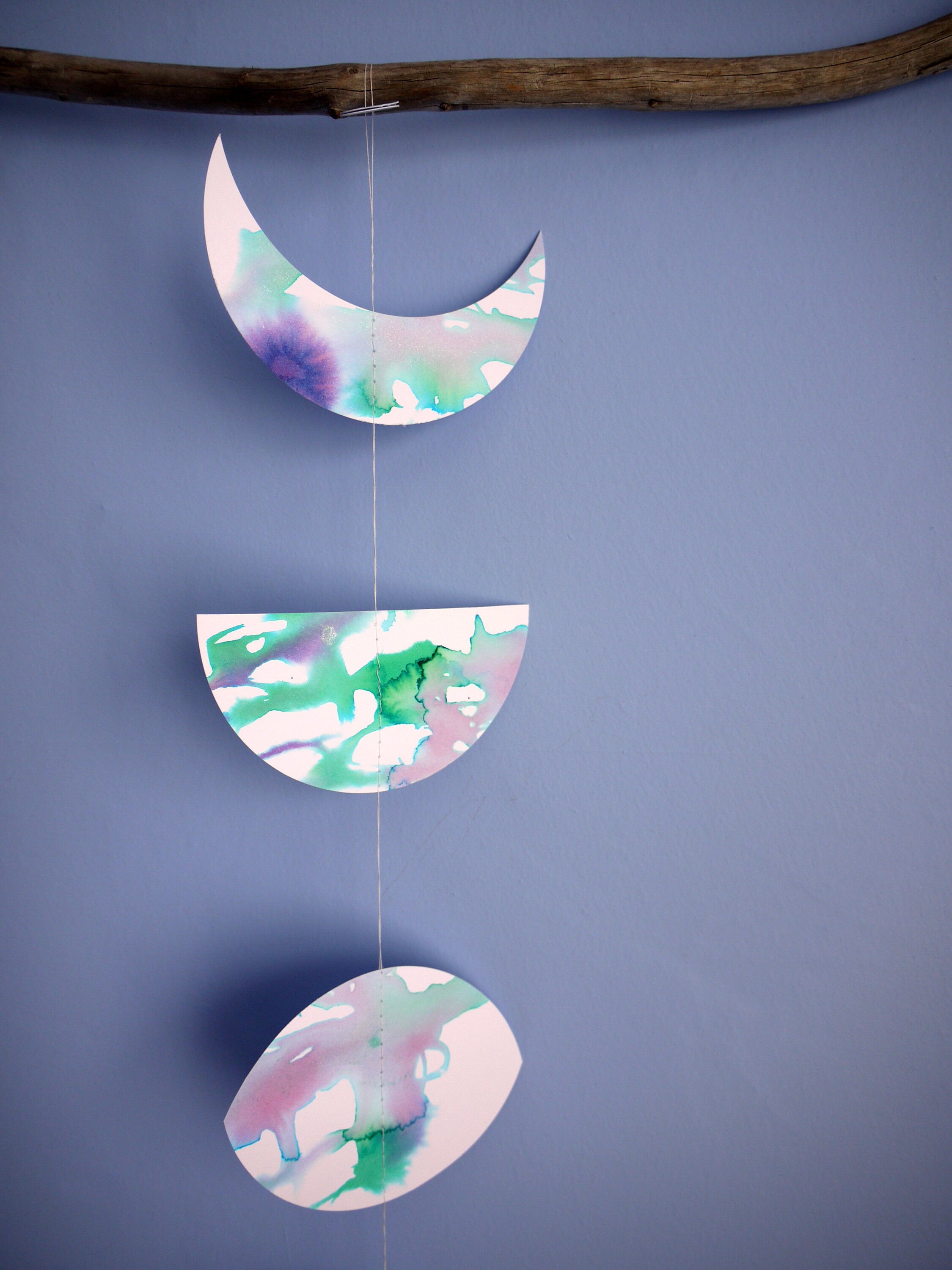 Close up of moon phase shapes painted with green and purple pearlised ink stitched to create a wall hanging displayed on a blue background