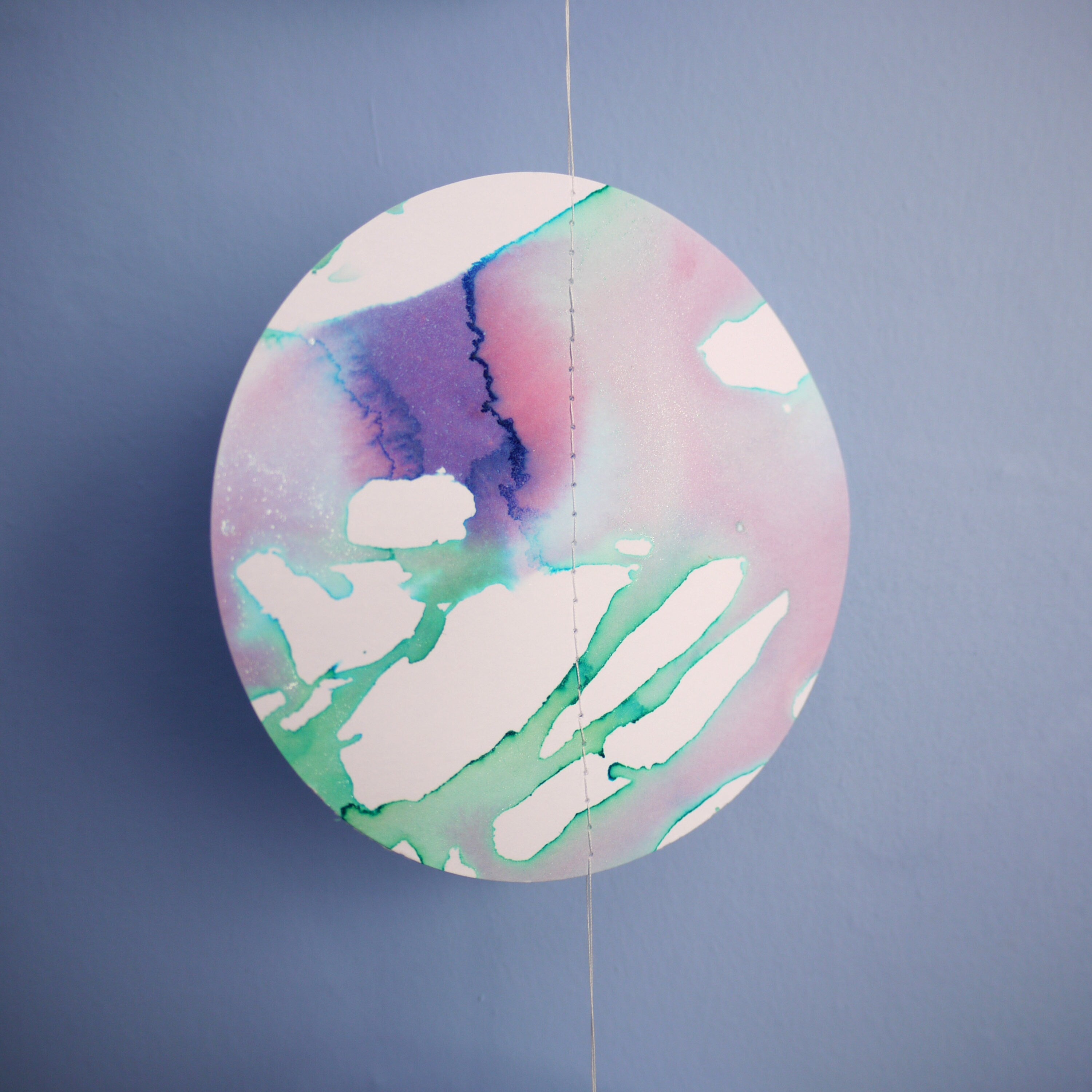 Close up of full moon phase shape painted with green and purple pearlised ink stitched to create a wall hanging displayed on a blue background