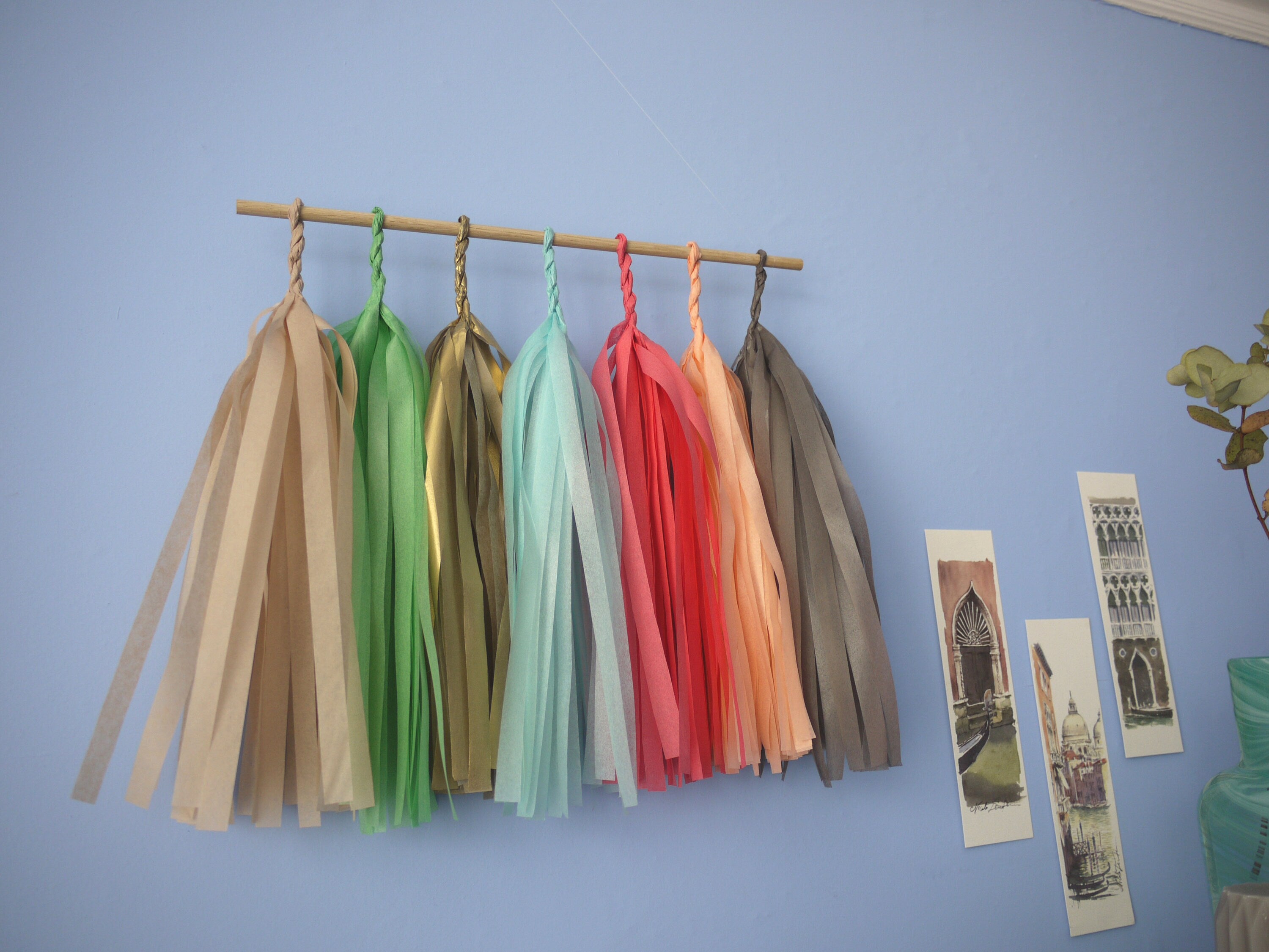Soft coloured tassel wall hanging on a blue wall beside some Venice illustrations and trinkets