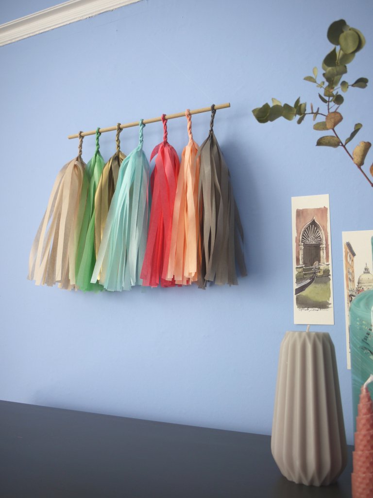 Soft coloured tassel wall hanging on a blue wall beside some Venice illustrations and trinkets