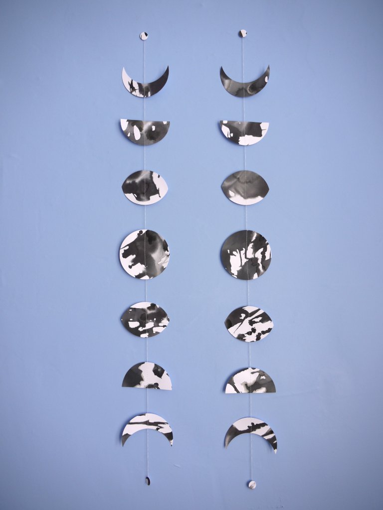 Decorative hanging mobile with moon phases on a blue background. Two paper garlands hang side by side for comparison of this unique handmade item