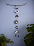 Decorative paper garland of moon shapes on a branch against a blue wall with plants.