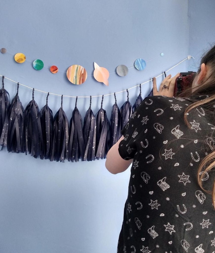 Artisan taking a photo of a decorative wall with tassels and colorful solar system wall hanging