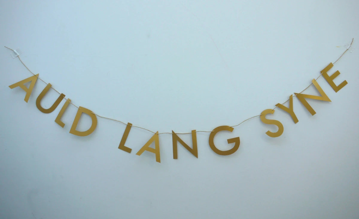 Gold paper banner reads AULD LANG SYNE. Scots phrase decor as New Year at home idea.