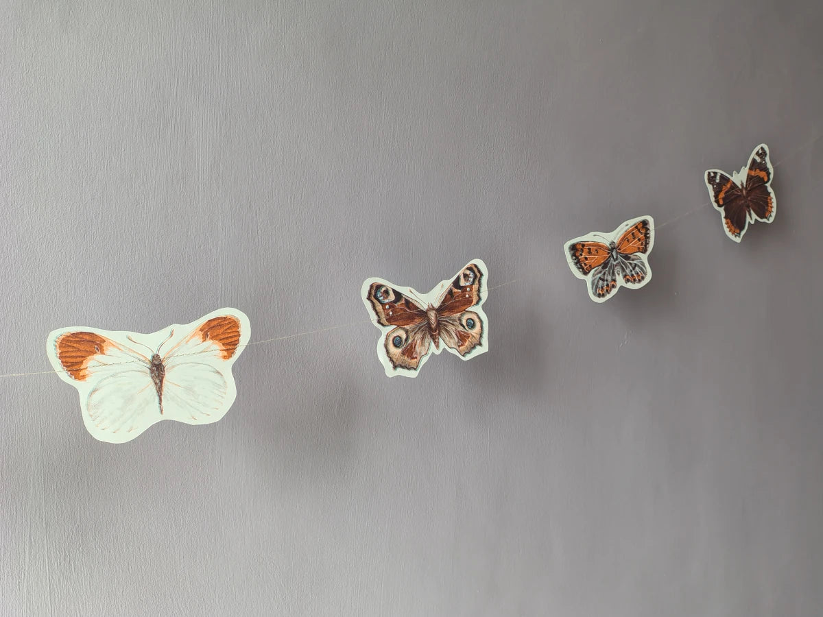 Four butterfly riso print shapes from a butterfly garland hanging on a wall as naturalist home decor.