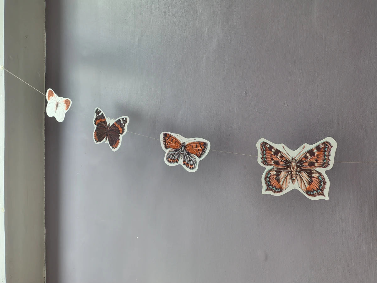 A butterfly garland hanging on a plain wall. Riso print naturalist home decor.