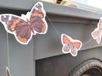 Close up on a butterfly riso print shape as part of a butterfly garland. Naturalist home decor hanging from a mantlepiece.