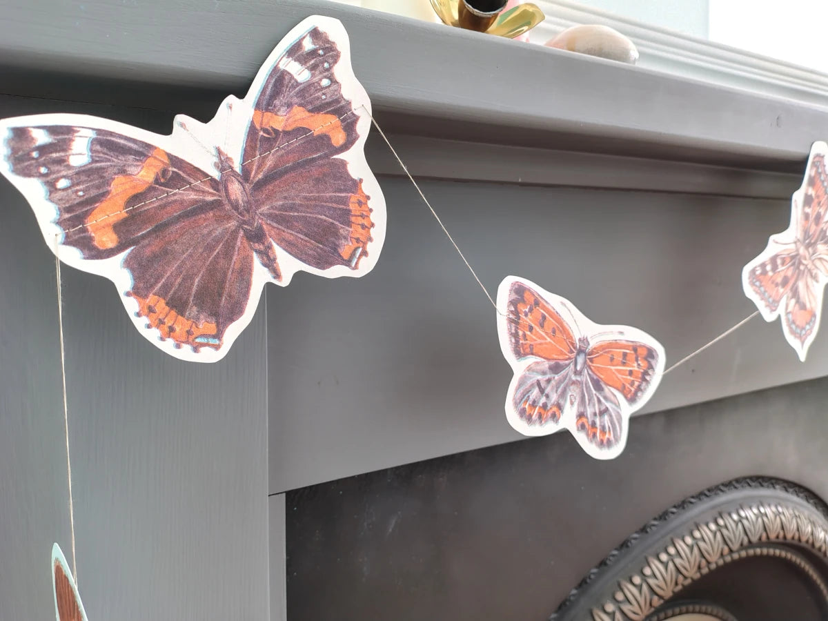 Close up on a butterfly riso print shape as part of a butterfly garland. Naturalist home decor hanging from a mantlepiece.